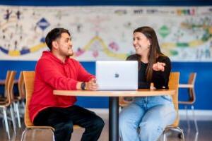 Two students smiling in front of a laptop computer at a table